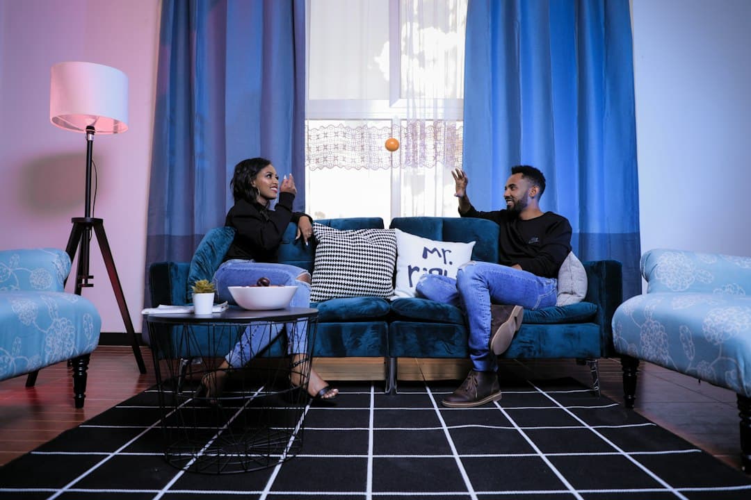 Two friends talking on a blue sofa at home, deciding which IPTV service to choose, such as Pixlar8k